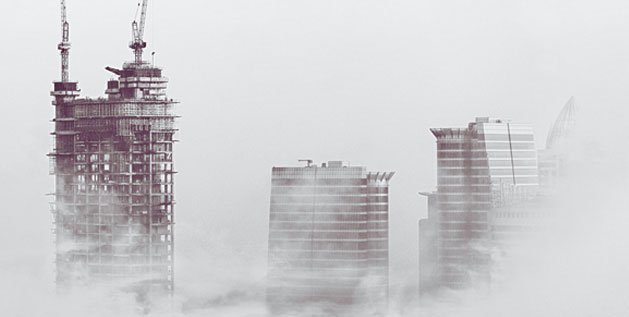 A skyscraper under construction in a foggy sky next to other buildings