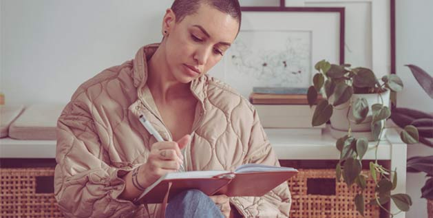 A woman sits with a notebook and is writing
