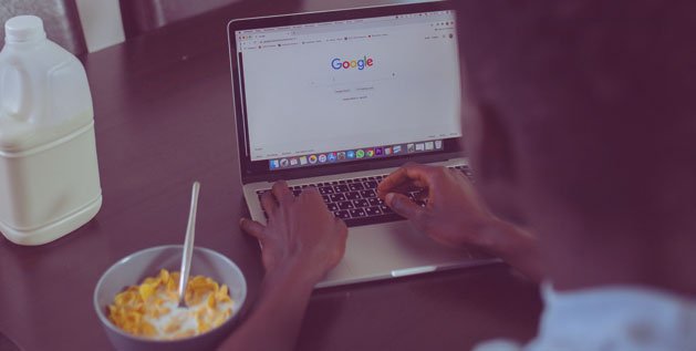 A man eats his breakfast while browsing Google on his Laptop