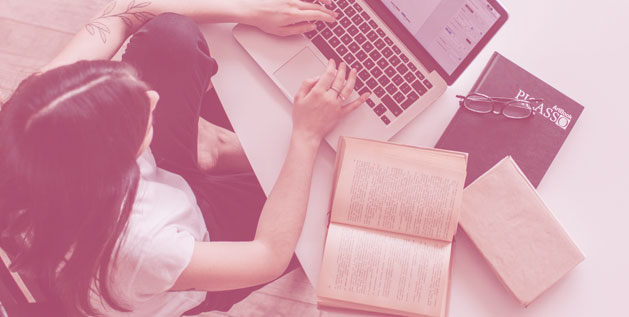 Woman types at a computer with books around her
